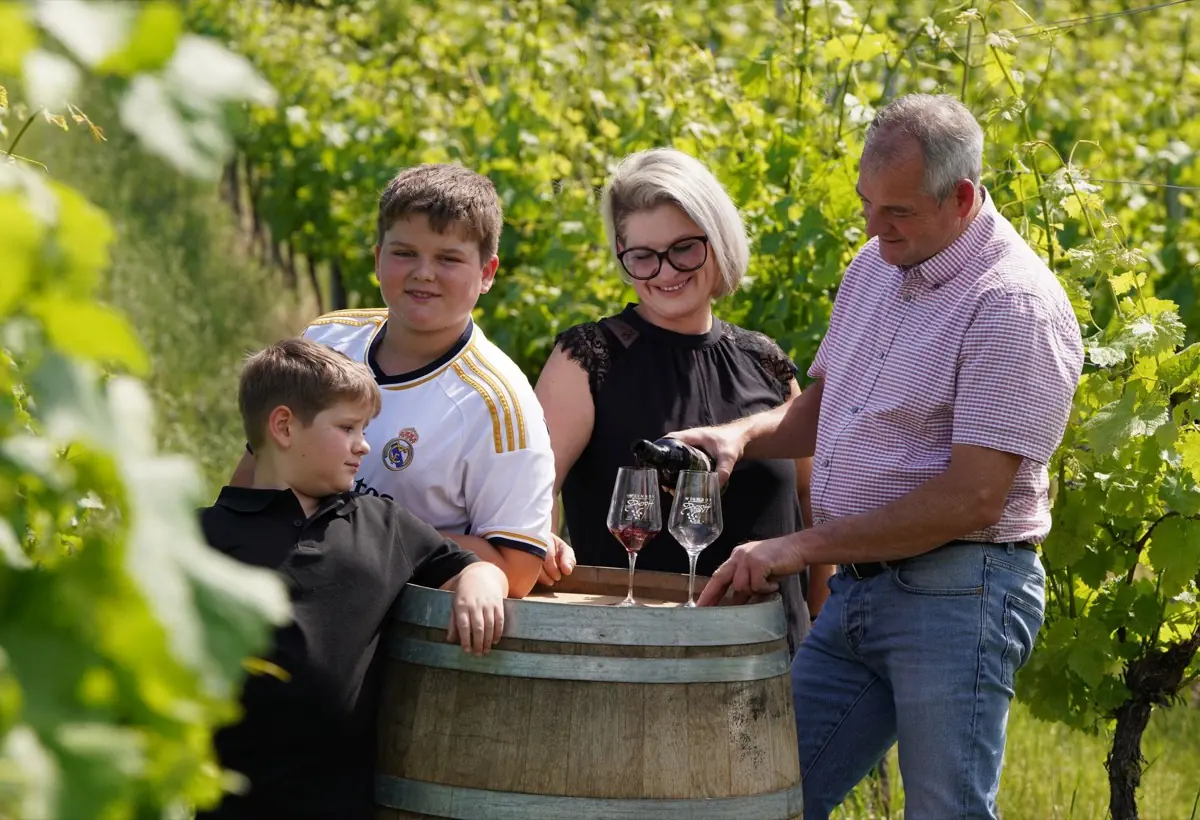 Rainer Dieroff schenkt Rotwein in zwei Gläser mit Weinhof-Dieroff-Gravur ein, die auf einem Holzfass im Weinberg stehen.