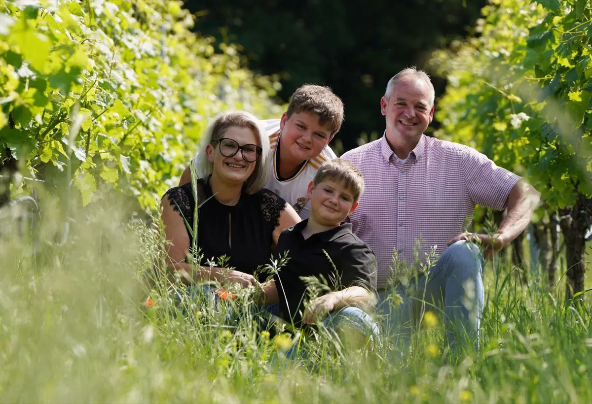 Die Familie Dieroff sitzt zwischen blühenden Gräsern in einer begrünten Rebgasse.