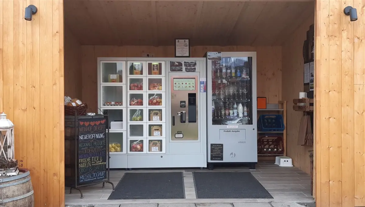 Der Verkaufsautomat des Weinhofs in einer Holzhütte: Fächer mit Eiern, Äpfeln und Nudeln, daneben ein Automat mit Wein- und Saftflaschen.
